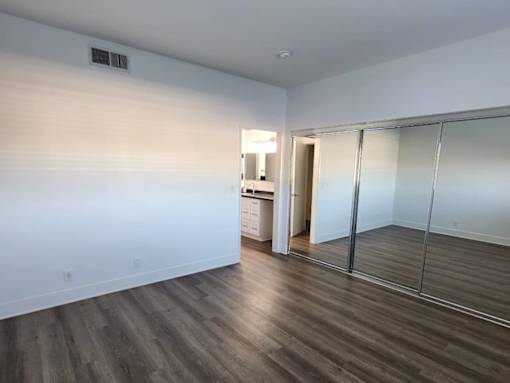 A room with wooden floors and a white wall with a doorway leading to another room.
