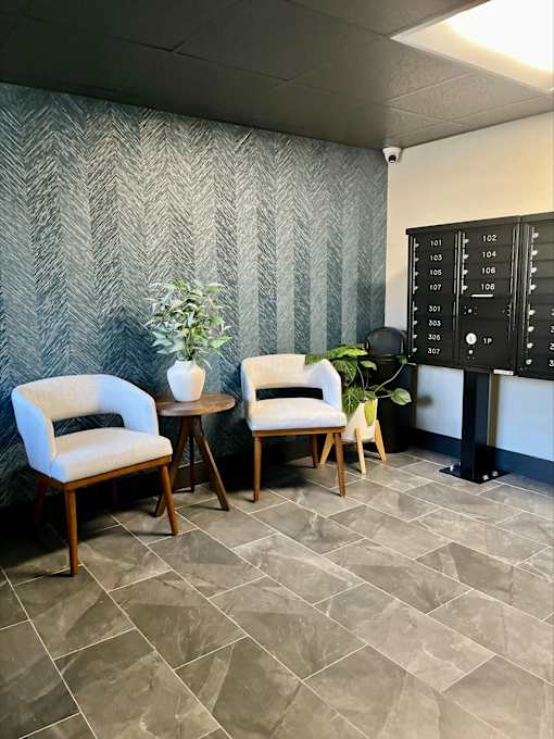 Two white chairs are placed in front of a grey wall with a black panel on the right side.