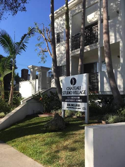 A sign for Chateau Studio Village is in front of a white building.