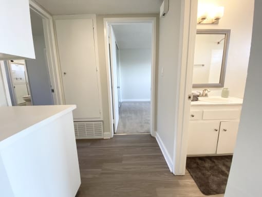 a bathroom with white cabinets and a hallway with a sink and a mirror