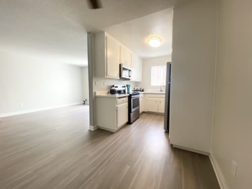 an empty living room and kitchen with wood floors and white cabinets
