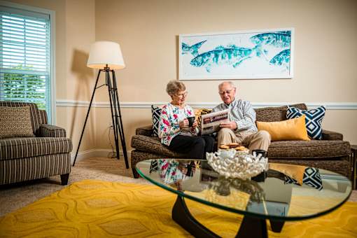 An older couple is sitting on a couch in a living room.