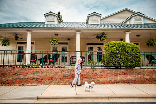 A woman walking her dog in front of a house with a green roof.