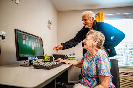 A man is helping an elderly woman with her computer.