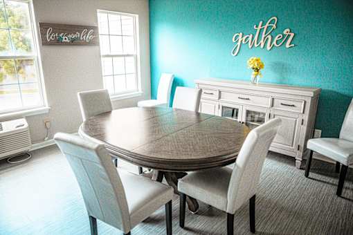 A dining room with a table and chairs and a wall decal that says "gather".