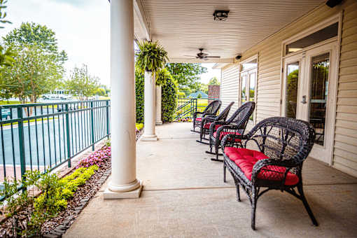 A row of black wicker chairs with red cushions are lined up on a porch.