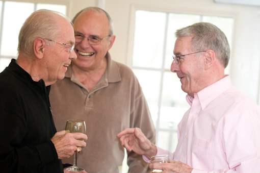 Three men are laughing and talking while holding drinks.