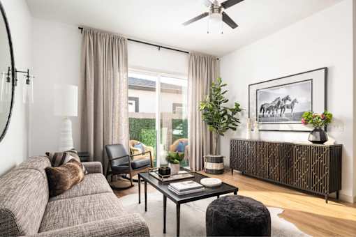 A living room with a grey couch, a black coffee table, a chair, a potted plant, a vase, a framed picture, and a window with curtains.