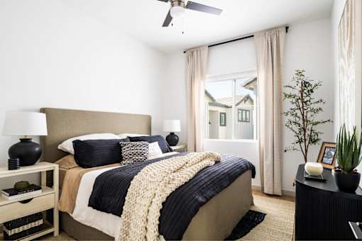 A bedroom with a bed, nightstand, and a plant.