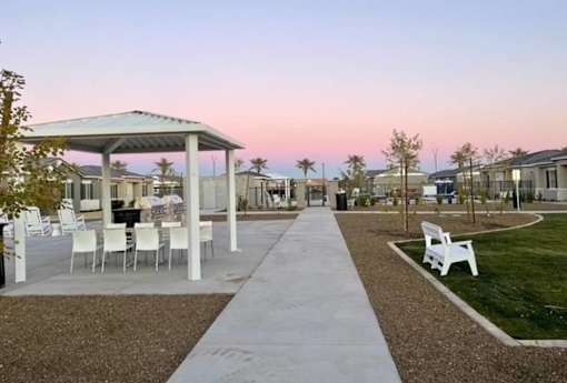 A gazebo with white chairs is surrounded by a gravel path and grassy area.