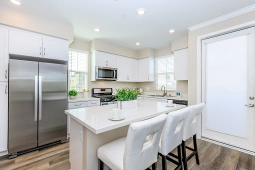 a white kitchen with stainless steel appliances and white chairs