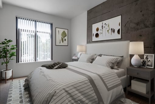 Apartments Near Santana Row - Vendome Place - Bedroom with Carpeted Flooring, Exposed Concrete Accent Wall, Large Bed, Nightstands with Lamps, Potted Plant, and Spacious Window.