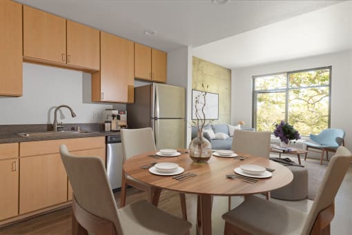 Downtown San Jose, CA Apartments - Vendome Place - Open Floor Plan Kitchen with Luxury Vinyl Tile Flooring, Stainless Steel Appliances, Brown Flat-Panel Cabinets, Round Dining Table with Chairs, and View of Living Area.
