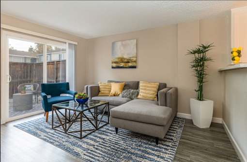 A living room with a grey couch, a blue chair, a coffee table, and a painting on the wall at Nola 624 Apartments, West Covina, California