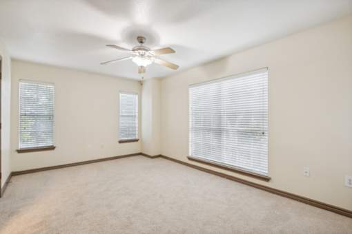 A room with a ceiling fan and two windows.