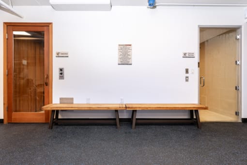 a wooden bench in front of a white wall with a door