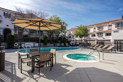 A poolside table and chairs are set up under a yellow umbrella.