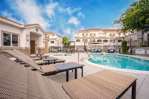 A pool area with sun loungers and a building in the background.
