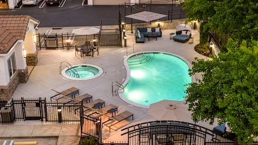 A pool area with two pools and a hot tub surrounded by a fence.