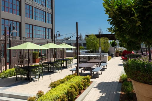 a patio with tables and umbrellas on a sunny day at Aqua Via Apartments, Oakland, 94607