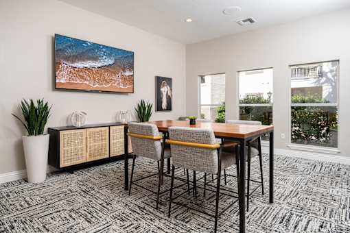 A room with a table, chairs, and a painting of a beach scene.