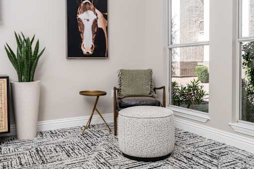 A living room with a chair, ottoman, and a picture of a horse on the wall.