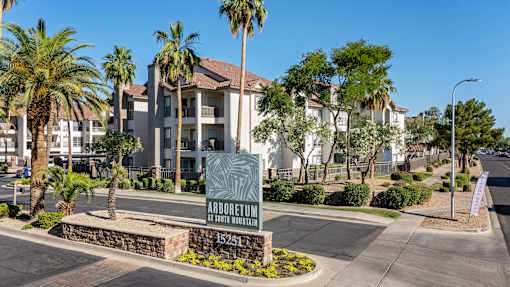 A sign for Arboretum Apartments is in front of a building with palm trees.