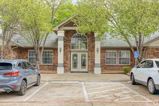 A parking lot in front of a brick building with two cars parked.