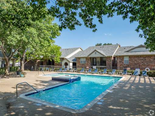 A swimming pool surrounded by trees and chairs in front of a house.