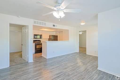 A living room with a ceiling fan and a kitchen area in the background.