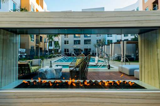 A modern outdoor pool area with a fire pit in the foreground. at Baker Block, Costa Mesa, CA, 92626