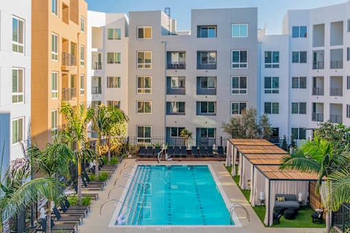 A swimming pool surrounded by lounge chairs and palm trees in front of apartment buildings. at Baker Block, Costa Mesa, CA