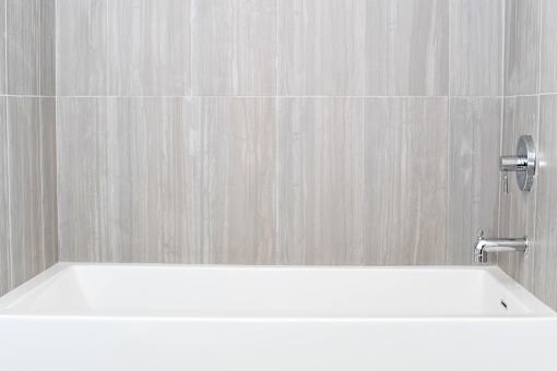A white bathtub in a bathroom with grey tiled walls at Wilshire Valencia Apartment, Los Angeles, CA