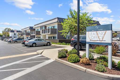 A leasing office sign is displayed in front of a building with a parking lot in the foreground.