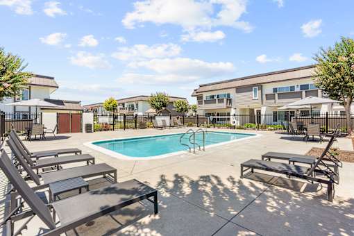 A pool with sun loungers and a building in the background.