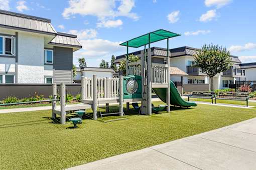A playground with a green slide and a white and grey building in the background.