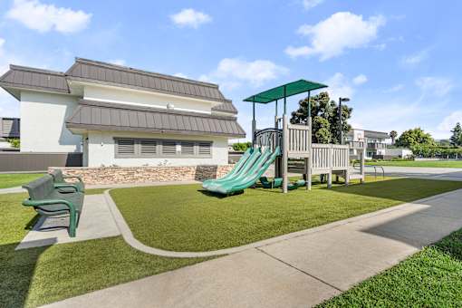 A playground with a green slide and a white building in the background.