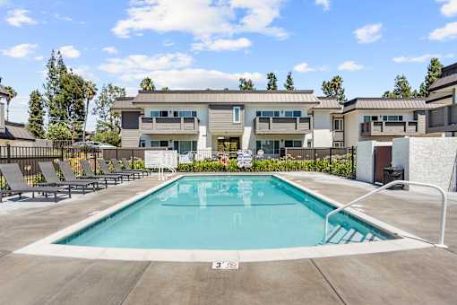 A swimming pool in front of a building with a fence and trees in the background.