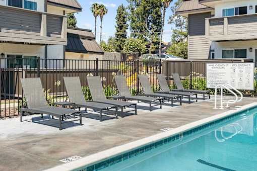 A pool with lounge chairs and a sign in front of apartment buildings.