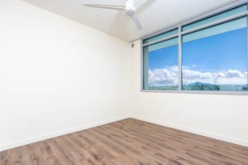 A room with a ceiling fan and a window showing a view of the sky and trees.