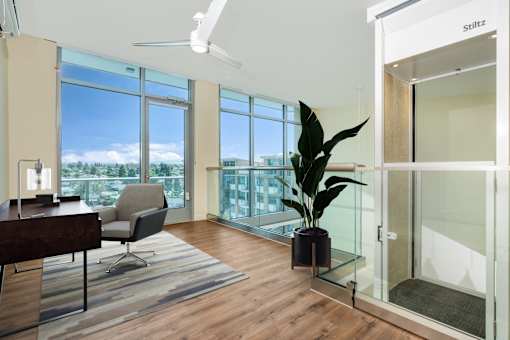 A room with a wooden floor, a chair, a table, a potted plant, and a ceiling fan.