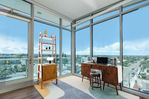 A room with a desk and chair in front of a large window with a view of the city.