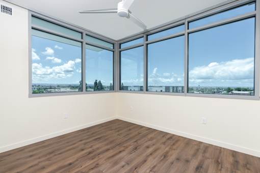 A room with a ceiling fan and large windows overlooking a cityscape.