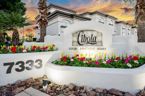 The image shows a sign for Cibola Luxury Apartment Homes with a number 7333 and a garden in front.