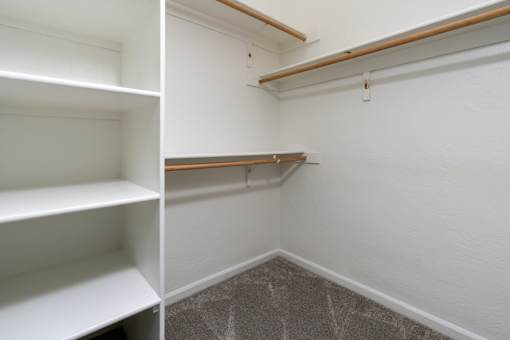 A white shelving unit with three shelves is in a room with white walls and a grey carpet.