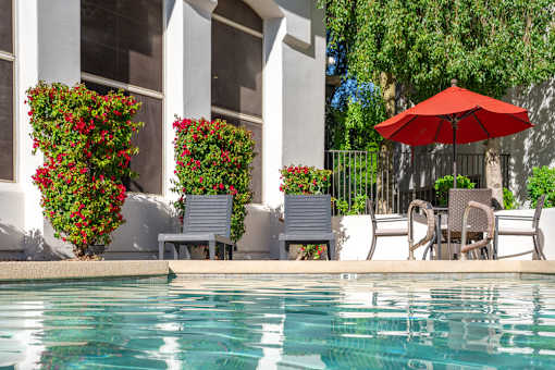 A pool with a red umbrella and chairs.