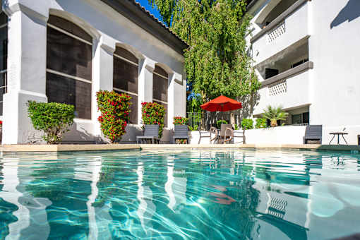 A pool with a red umbrella and chairs in front of a white building.