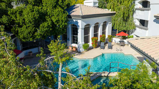 A pool surrounded by trees and a white building with columns.
