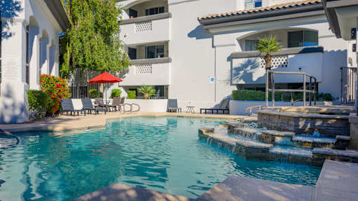 A pool with a red umbrella and a white building in the background.