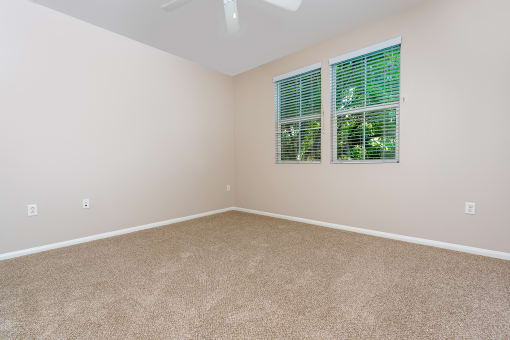 a bedroom with beige carpet and two windows